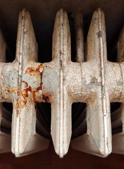 A close-up photo looking down on an old white radiator with spots of rust and chipped paint.
